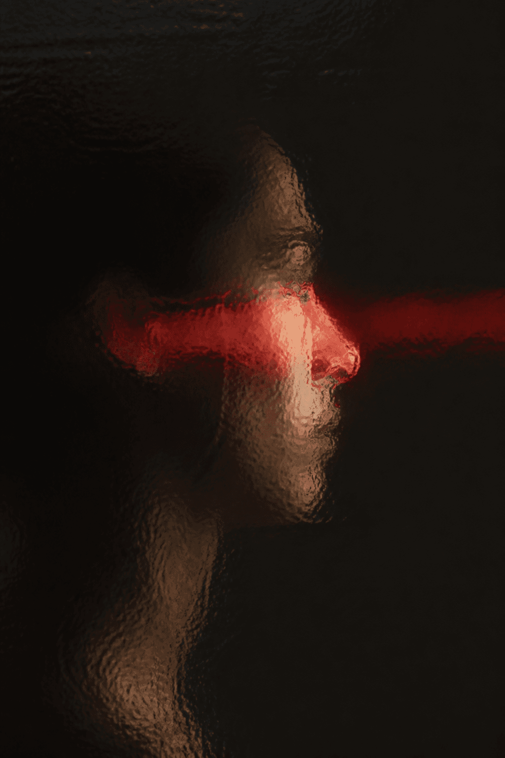 Profile silhouette distorted through glass and crossed by red light