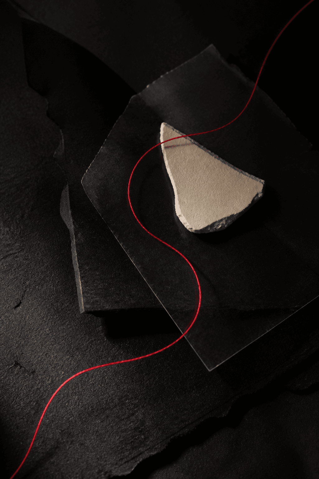 Red thread tracing a path through black paper and a bone-white fragment